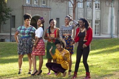 Six models standing on grass in front building